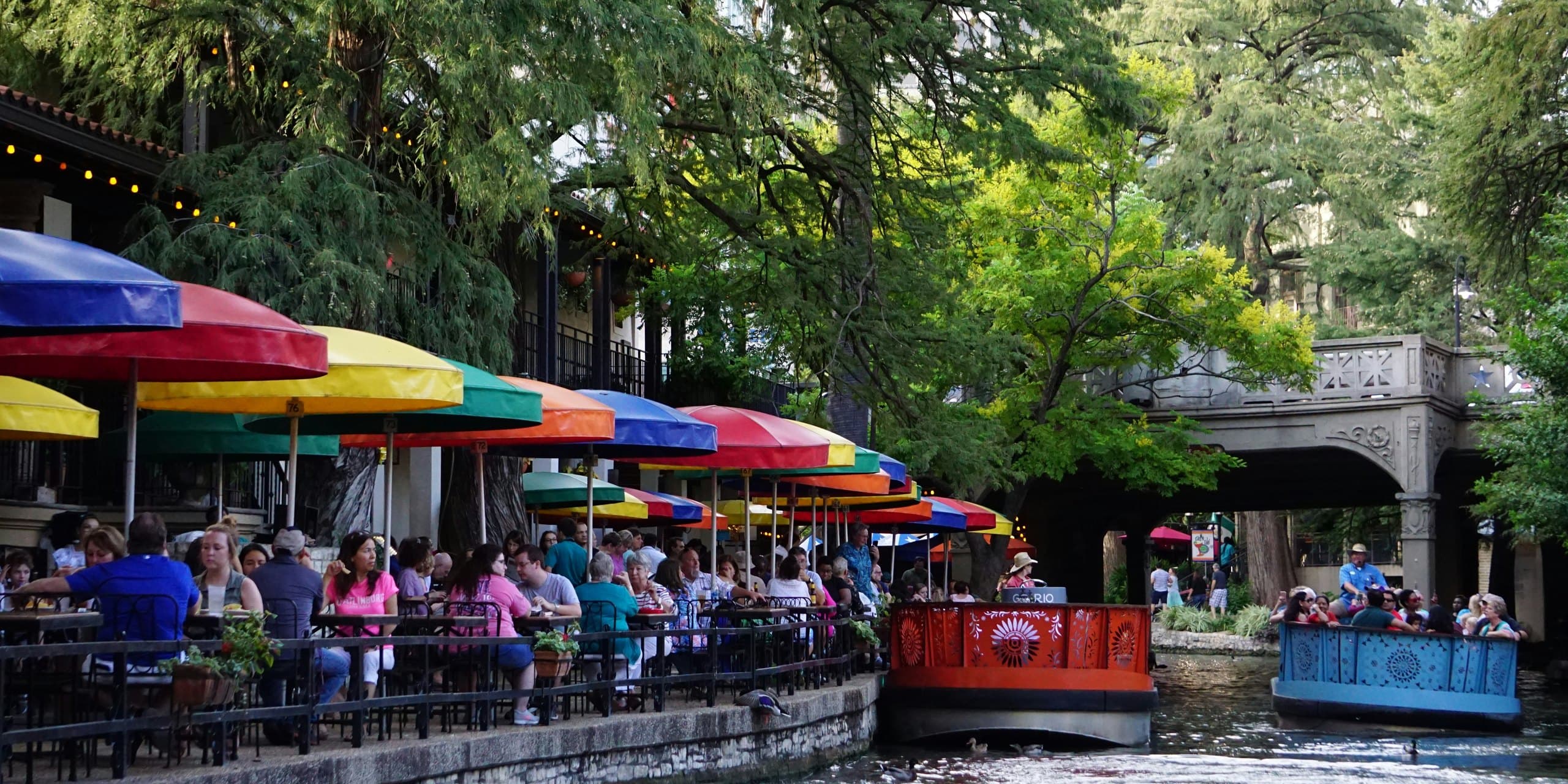 The San Antonio River Walk on a sunny day, with colourful café umbrellas and river boats